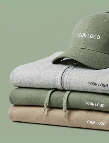 Bild Gestapelte Hoodies in Grau, Gr�n und Beige, darauf eine gr�ne Cap, jeweils mit Logo-Platzhalter