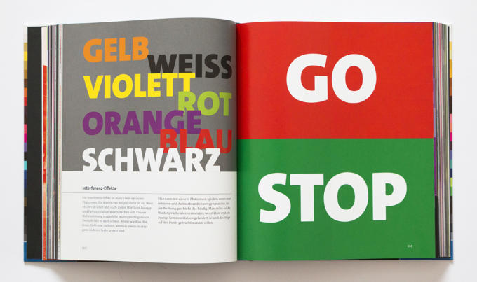 Ein aufgeschlagenes Buch offenbart fettgedruckten Text über zwei Seiten. Links zeigt „Das ABC der Farbe“ deutsche Farbnamen in leuchtenden Farben. Auf der rechten Seite steht „GO“ in Weiß auf rotem Hintergrund und „STOP“ in Weiß auf grünem Hintergrund.