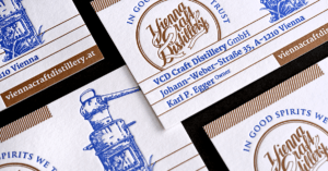 Visitenkarten der Vienna Craft Distillery zeigen eine Illustration eines blauen Vintage-Destillierapparats, die im Buchdruckverfahren hergestellt wurde. Das Logo „Vienna Craft Distillery“ ist in eleganter Schrift gehalten. Kontaktdaten: Website und Adresse: Johann-Weber-Straße 35A, Wien.