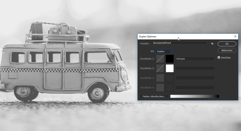 Vor einem unscharfen Hintergrund ist ein Graustufenbild eines alten Spielzeug-Vans mit Dachgepäckträger und Gepäck zu sehen. Rechts darüber ist ein digitales Bearbeitungsfenster mit Duplex-Optionen, das an Photoshop erinnert, eingeblendet, in dem Sepia-Farbanpassungen auf Deutsch angezeigt werden.