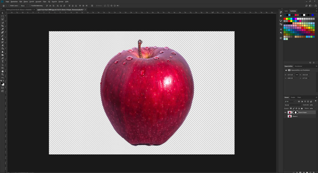 Ein roter Apfel mit Wassertropfen wird vor einem transparenten Hintergrund in einem Photoshop-Arbeitsbereich angezeigt. Die Benutzeroberfläche zeigt verschiedene Symbolleisten und Ebenen, die den Bildbearbeitungsprozess verdeutlichen.