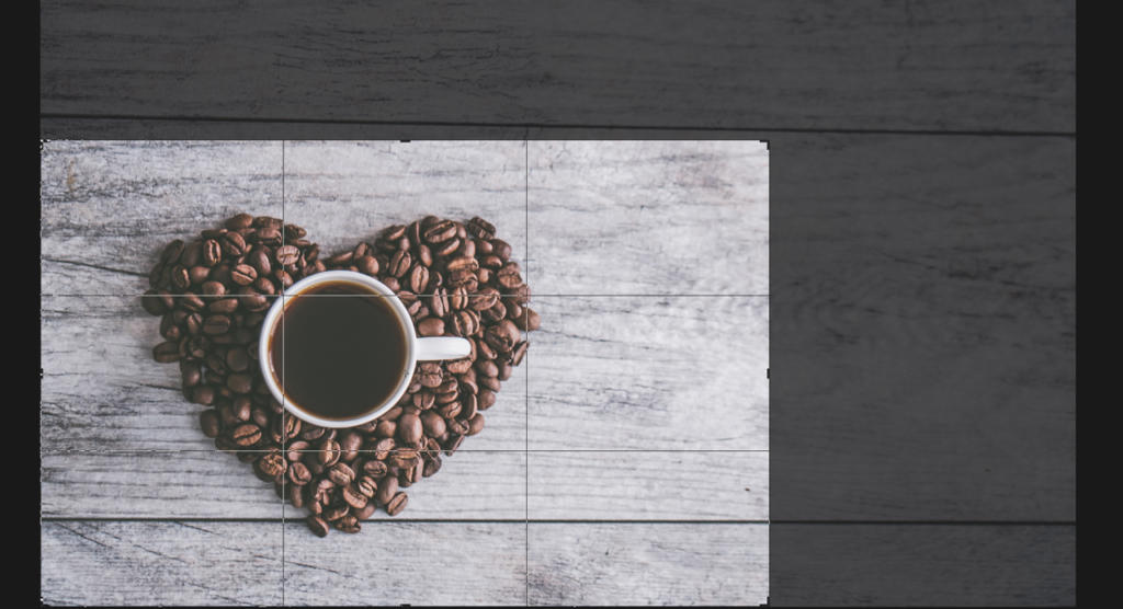 Eine Tasse Kaffee steht auf einer Holzoberfläche, umgeben von herzförmig angeordneten Kaffeebohnen. Der Hintergrund ist eine rustikale Holzstruktur, die eine gemütliche Atmosphäre schafft.