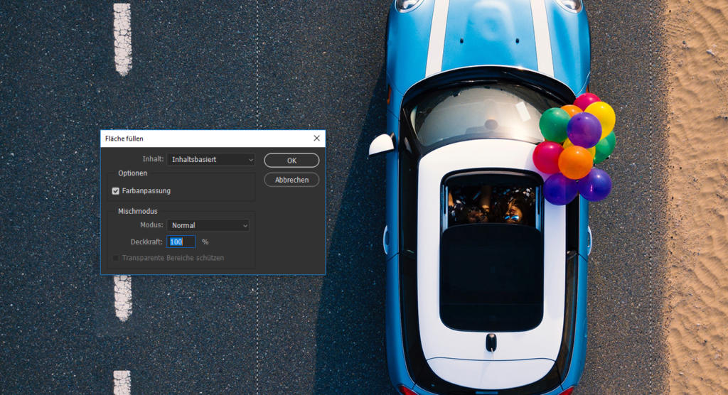 Eine Luftaufnahme zeigt ein blaues Cabrio auf einer Sandstraße. An der Beifahrerseite sind bunte Luftballons befestigt. Auf der linken Bildseite ist ein Photoshop-Oberflächenfenster eingeblendet, das Kreativität mit Realität verbindet.