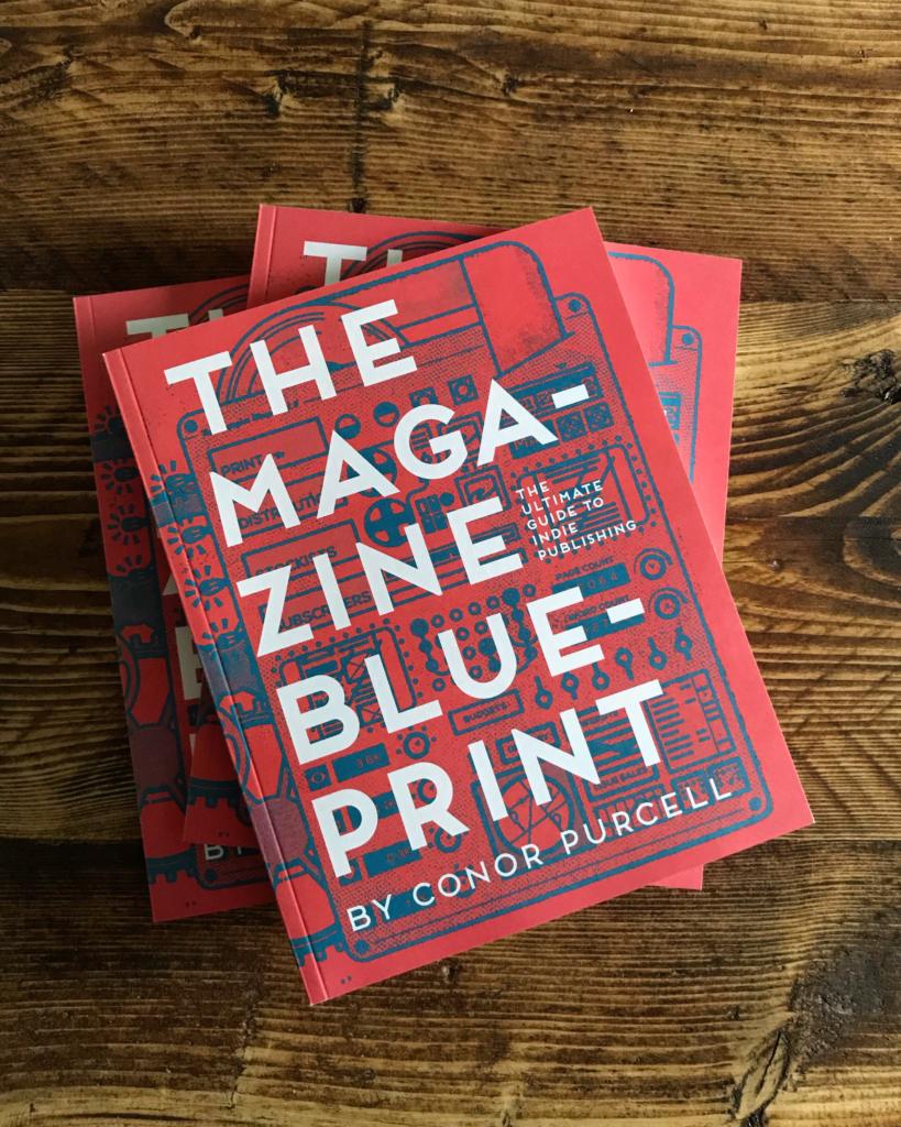 Cover des Buches „The Magazine Blueprint“ von Conor Purcell. Es zeigt einen roten Hintergrund mit blauen Skizzen von Verlagsgeräten. Das Buch liegt auf einer Holzoberfläche.