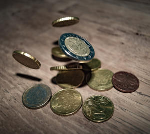 Verschiedene Münzen liegen in der Luft und verstreut auf einer Holzoberfläche. Die Münzen, ähnlich einem effizienten Beschwerdemanagementsystem, sind überwiegend gold- und silberfarben, in unterschiedlichen Größen und Designs gehalten und suggerieren so einen vielfältigen Währungsmix. Sanftes Licht hebt die metallischen Texturen hervor.