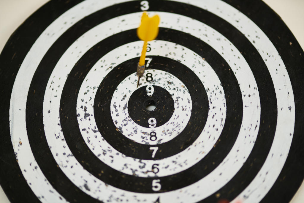 Eine Dartscheibe mit konzentrischen schwarzen und weißen Kreisen veranschaulicht präzises Zielen im Beschwerdemanagement. Ein einzelner gelber Pfeil sitzt perfekt in der Zielscheibe, umgeben von Zahlen, die die verschiedenen Punktebereiche anzeigen.