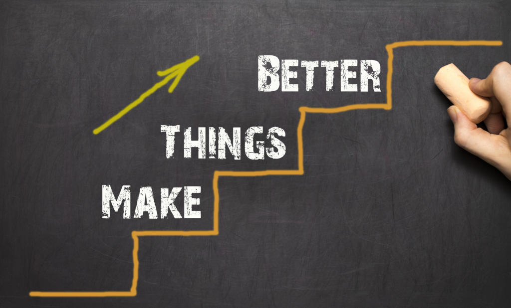 Eine Hand zeichnet mit Kreide ein Stufendiagramm auf eine Tafel. Die Worte „MAKE THINGS BETTER“ begleiten jeden Schritt und symbolisieren effektives Beschwerdemanagement. Ein nach oben zeigender gelber Pfeil verdeutlicht den Weg des Fortschritts und der Verbesserung.
