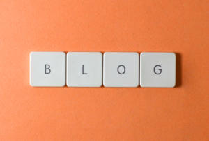 Auf einem orangefarbenen Hintergrund sind vier Tastaturtasten mit der Aufschrift „BLOG“ aufgereiht, die die Kunst des Content-Marketings in den Vordergrund rücken.