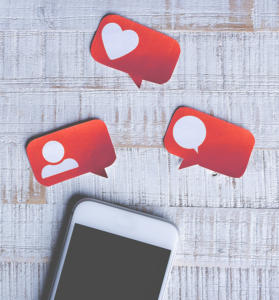 Ein Smartphone liegt auf einer Holzoberfläche, die mit roten Sprechblasen-Symbolen verziert ist. Diese Symbole – ein Herz, eine Personensilhouette und eine leere Sprechblase – imitieren Social-Media-Benachrichtigungen und verkörpern die Essenz des Content-Marketings im heutigen digitalen Zeitalter.