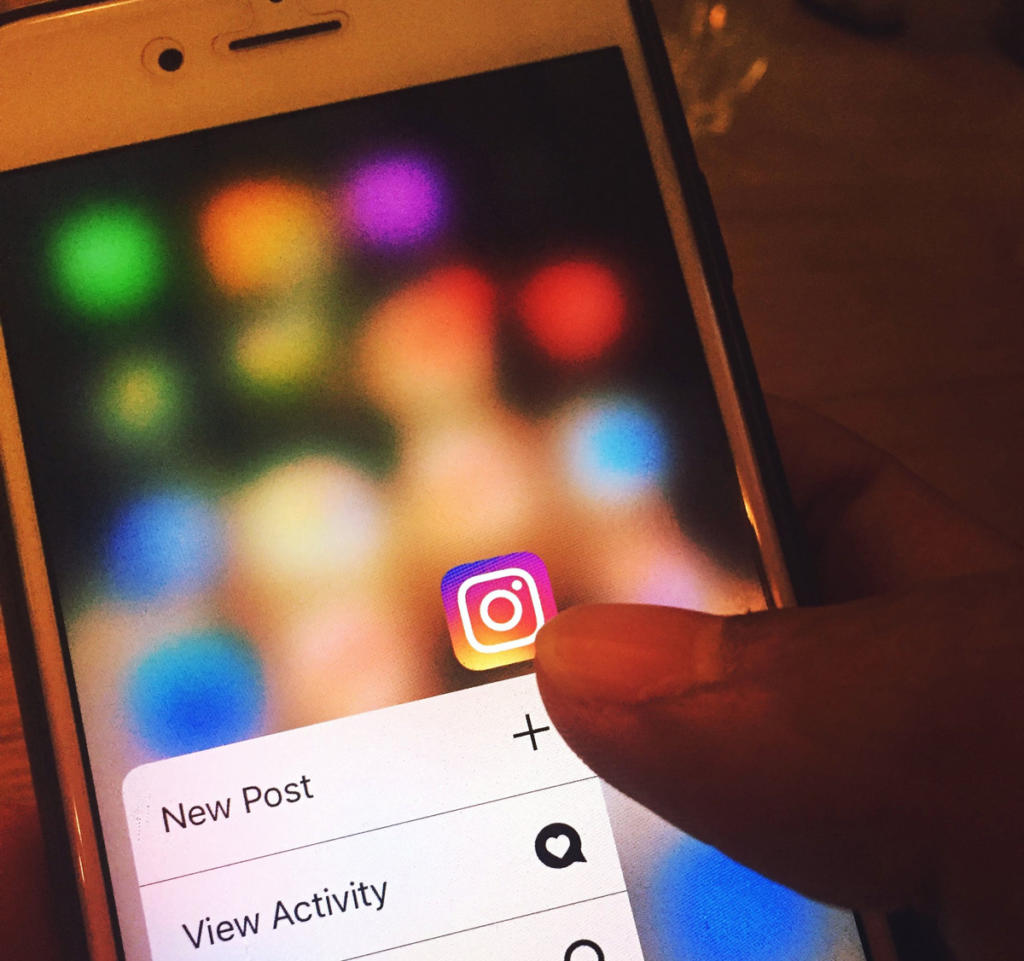 Auf dem Smartphone-Bildschirm wird das Instagram-App-Symbol angezeigt, umgeben von verschwommenen Symbolen – einsatzbereit. Ein Fingertipp öffnet Optionen wie „Neuer Beitrag“ und „Aktivität anzeigen“ – perfekte Tools für Eventmarketing mit einer nahtlosen Mischung aus Visualisierung und Interaktion.