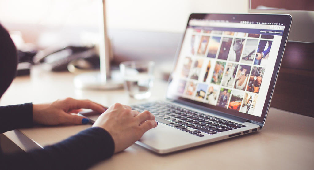 Eine Person nutzt einen Laptop auf einem Holzschreibtisch und erkundet eine Event-Marketing-Galerie. Im Hintergrund sind ein Glas Wasser und eine Lampe leicht unscharf. Die Umgebung wirkt sauber und organisiert und vermittelt den Eindruck eines produktiven Arbeitsplatzes.