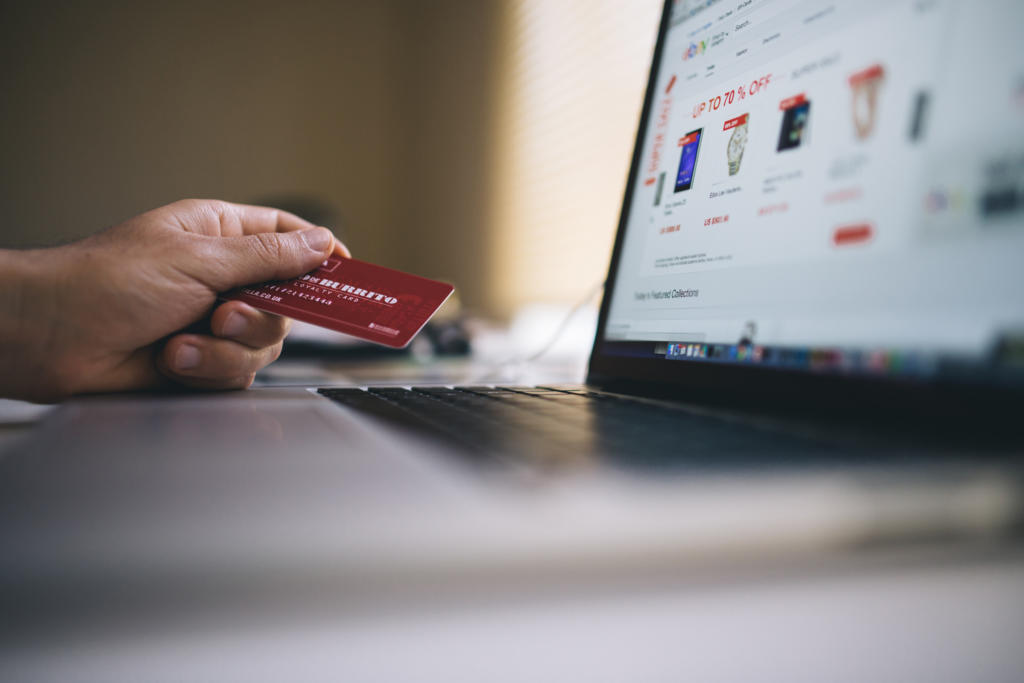 Eine Person hält eine rote Kreditkarte in der Hand, während sie online am Laptop einkauft. Das fördert die Kundenbindung. Der Bildschirm zeigt eine Shopping-Website mit verschiedenen Produkten, die das Interesse der Kunden wecken. Die entspannte Atmosphäre im Innenbereich ist ideal zum Stöbern und zur Stärkung der Markentreue.