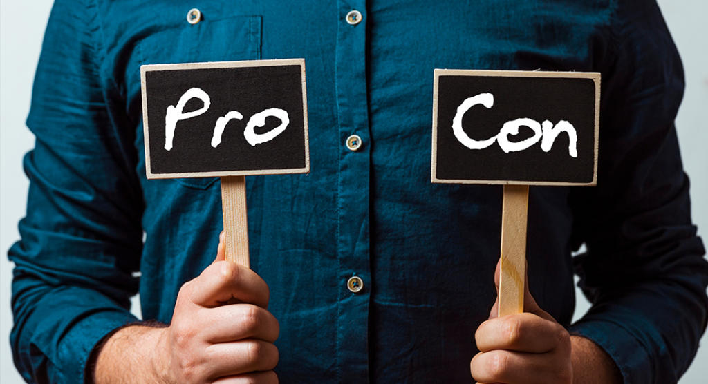 Eine Person in einem blauen Hemd, möglicherweise von einer Eventagentur, hält zwei kleine Schilder hoch. Auf dem linken Schild steht „Pro“ und auf dem rechten „Contra“. Beide stehen auf einem schlichten schwarzen Hintergrund mit auffälliger weißer Schrift.