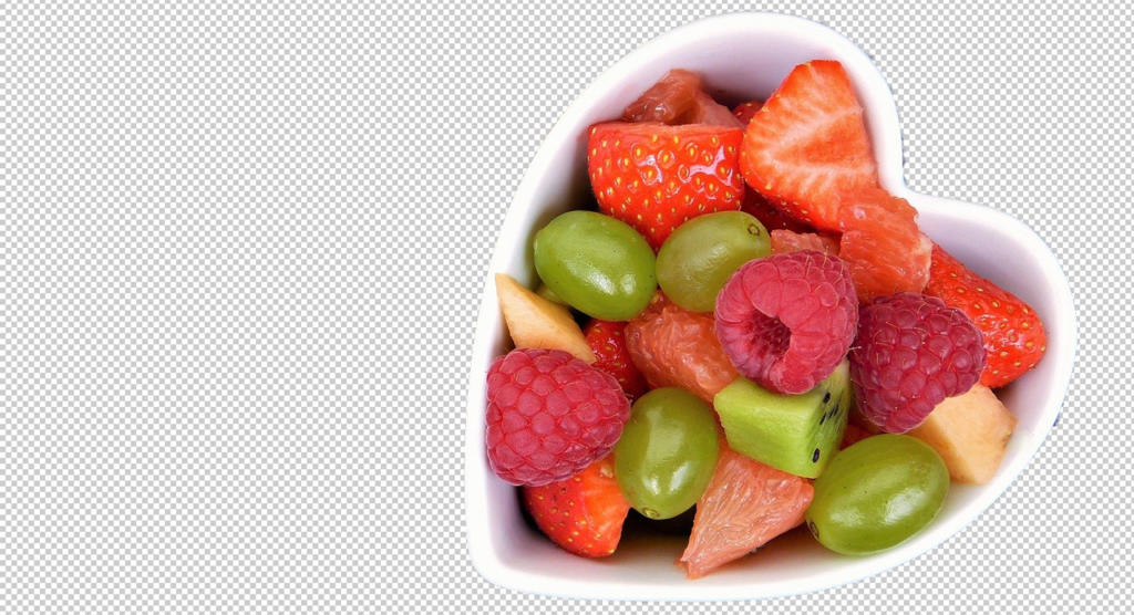 Eine herzförmige Schüssel, randvoll mit einer bunten Mischung aus Erdbeeren, Himbeeren, Kiwis, grünen Weintrauben und Apfelwürfeln, sticht vor einem transparenten Hintergrund hervor – ein Arrangement, das so makellos ist, dass es von Photoshop-Sensei-KI erstellt worden sein könnte.