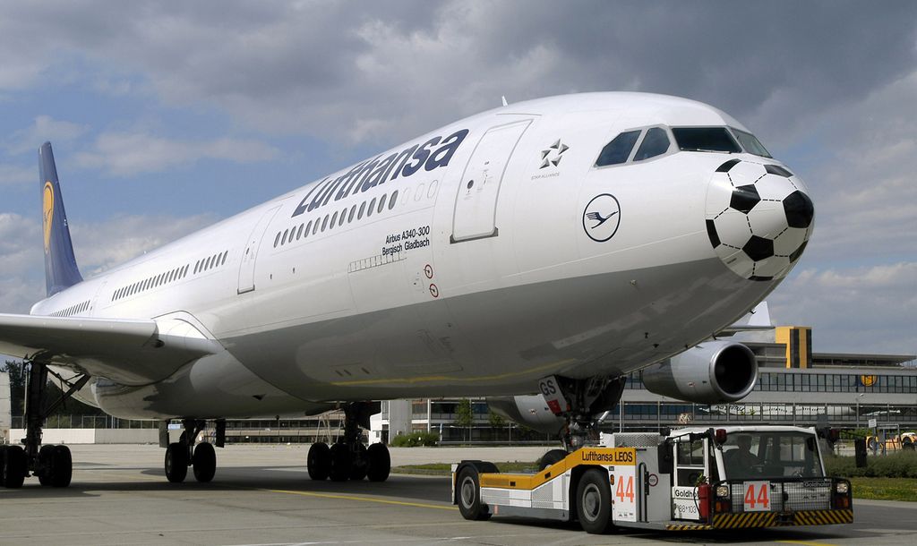 Ein Flugzeug mit einem Fußball-Motiv auf der Nase – ein cleverer Guerilla-Marketing-Ansatz – wird von einem Fahrzeug über die Landebahn des Flughafens gezogen. Der Himmel ist bewölkt, im Hintergrund ragt ein Flughafengebäude empor.