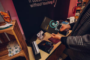 Eine Person in einer karierten Jacke hält ein Buch mit dem Titel „Doina Ioanid: Te spun iar de la început“ in der Hand. In der Auslage sind weitere Bücher und Preisschilder zu sehen. Im Hintergrund steht auf einer Tafel: „Es macht nichts, wenn du es zerbrichst, ohne es zu berühren.“.