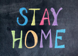 Die Worte „Stay Home“ sind mit bunter Kreide auf eine Tafel geschrieben. Jeder Buchstabe hat eine andere Farbe, darunter Blau, Gelb, Rosa, Lila, Grün und Orange. Der Hintergrund wirkt strukturiert und wirkt wie eine Tafel.