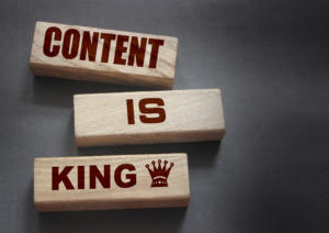 Drei Holzklötze auf grauem Hintergrund bilden den gekonnten Ausdruck „Content is King“. Darunter befindet sich eine kleine Krone, die die königliche Bedeutung eines ansprechenden Kundenmagazins unterstreicht.