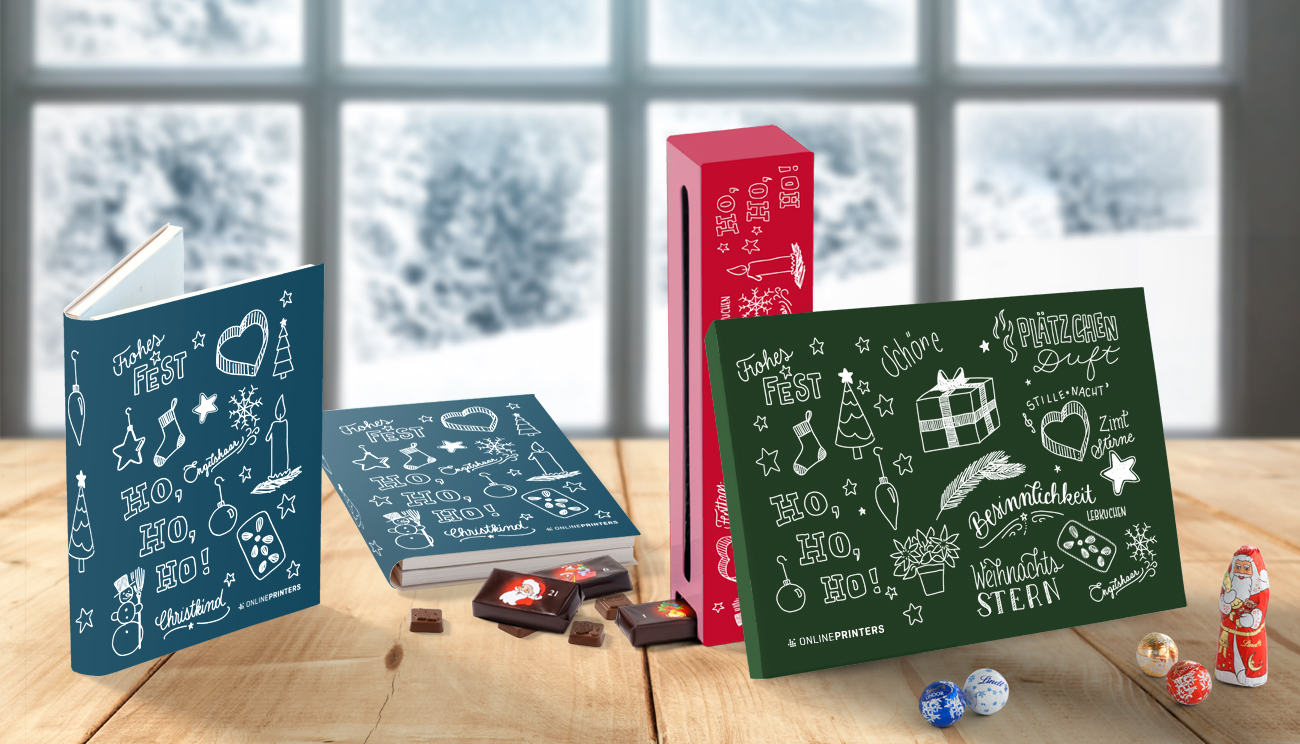 Drei festliche Schokoladen-Geschenkboxen mit weihnachtlichen Motiven und Kritzeleien sind kunstvoll auf einem Holztisch neben einem frostigen Fenster präsentiert und versprühen den Charme eines Adventskalenders. Die Boxen in Blau-, Rot- und Grüntönen sind von verschiedenen Pralinen und einer verschwommenen Winterlandschaft umgeben.