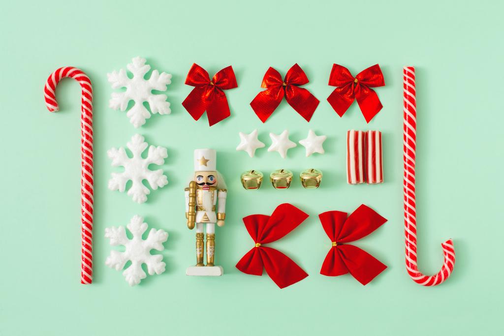 Feiertagsartikel, ordentlich auf mintgrünem Hintergrund angeordnet. Enthält Zuckerstangen, Schneeflocken- und Sternkekse, einen Nussknacker, goldene Glöckchen und rote Bänder.