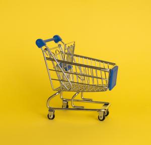 Ein Miniatur-Einkaufswagen mit blauen Akzenten steht vor einem leuchtend gelben Hintergrund und betont sein kompaktes Design und den Metallrahmen. Er eignet sich ideal für Gutschein-Textvorlagen und hebt Werbeangebote kreativ und stilvoll hervor.
