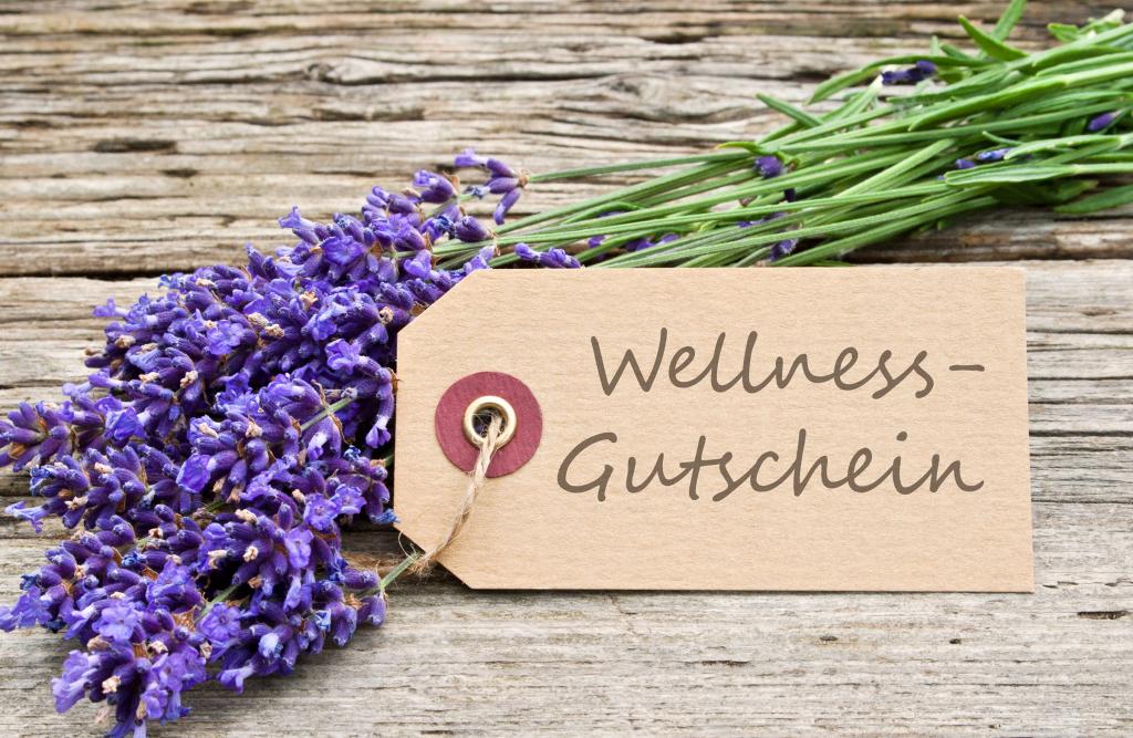 Auf einer Holzoberfläche ruht ein Lavendelstrauß, begleitet von einem braunen Etikett. Auf dem Anhänger, der an Gutschein-Textvorlagen erinnert, steht handschriftlich „Wellness-Gutschein“ und deutet damit auf einen entzückenden Wellness-Geschenkgutschein hin.